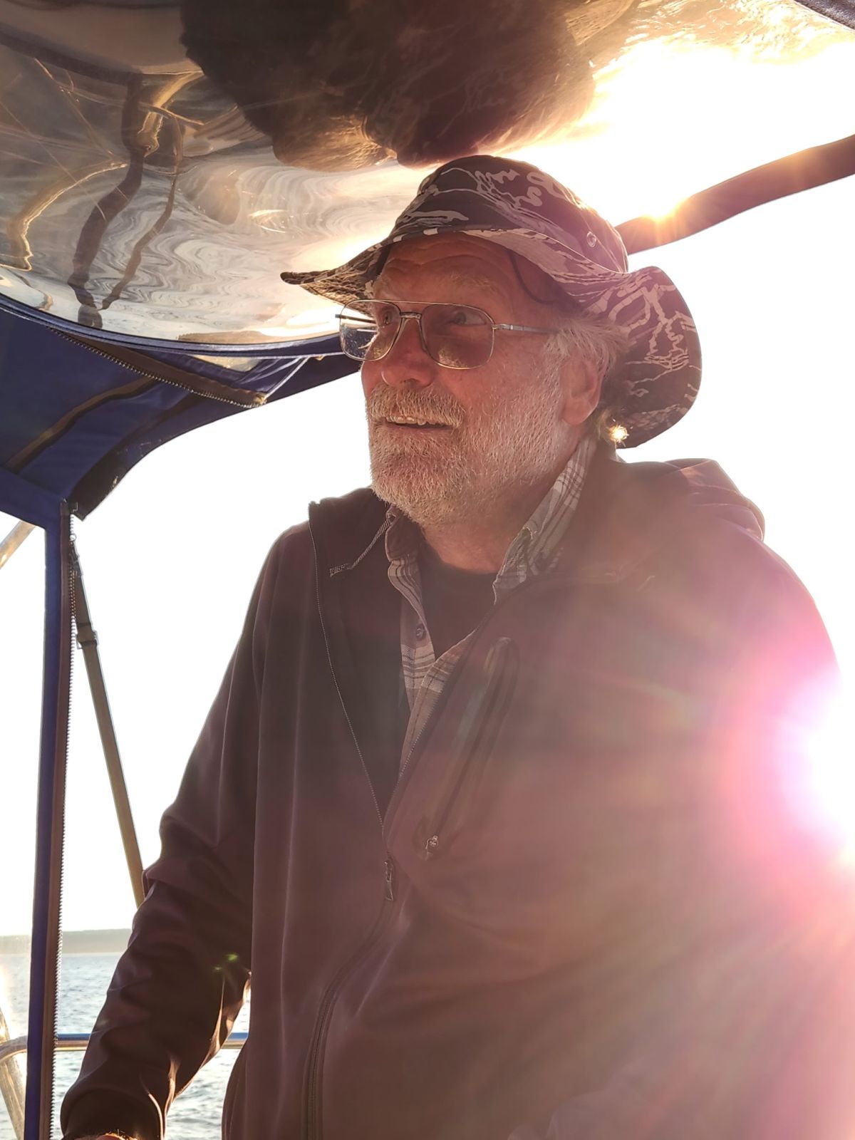 Person wearing a hat and glasses on a boat with sunlight in the background.